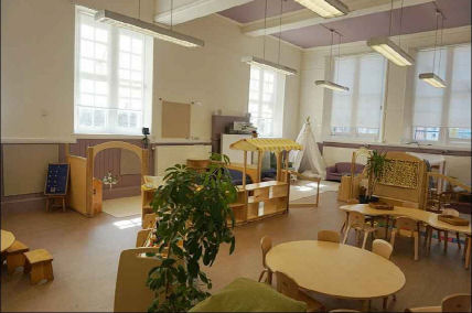 the classroom is laid out in well defined zones, a round table, a home area, a cozy corner