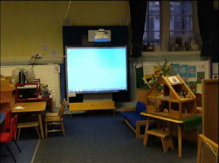 a Smart Board on the wall, in front of it is a small bench, chairs and tables