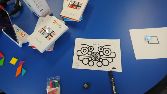 Ozobot is a line following robot shown in the image with it's blue light as it follows a square track drawn out on paper.