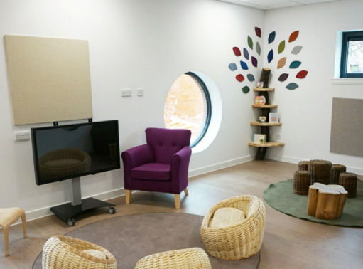 The teaching space in front of the interactive screen, a purple armchair for the teacher and wicker baskets on a rug for the children to sit at