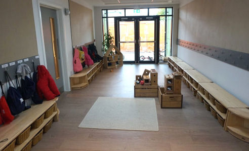 the cloakroom with baskets for shoes under benches and pegs at child height