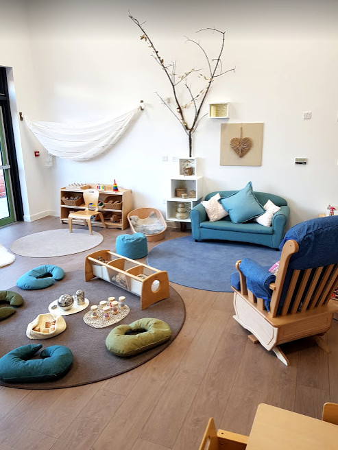 the cozy seating area looks like a living room with an adult rocking chair, sofa, floor cushions and three circular rugs