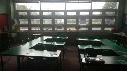 the tables and chairs are green, the tables are rectangular and have been laid out like two capitol letter E's facing eachother