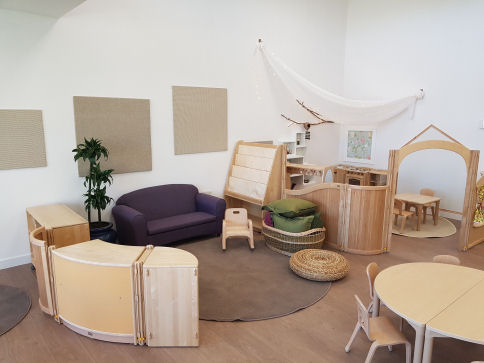 the reading area is cosy and looks like a living room with a sofa, a small rocking chair, cushions and shelving with a rug in the centre.