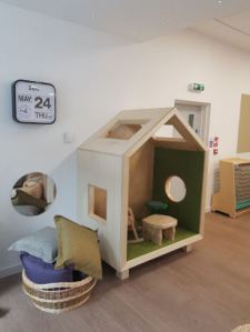 A house shaped nook with a rocking chair and small table inside enough for two children to sit in