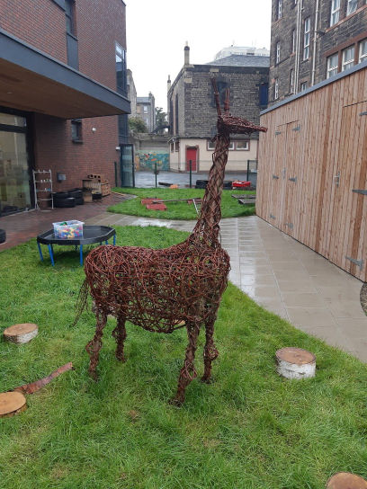outside in the garden are little log seats and a sculpture of a giraffe