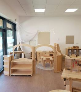 Home corner with a play kitchen and table with chairs is accessed through a small archway. a construction area with a workbench.