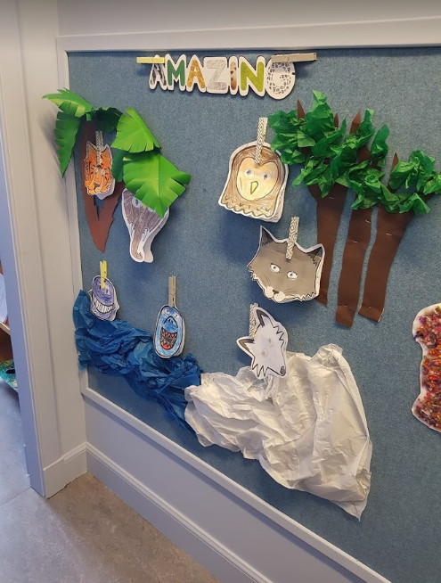 textured blue pinboard with a display of children's work, there are trees and animals
