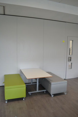 A flexible booth, two upholstered ottomans with wheels create seating at a table