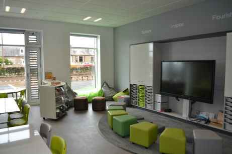 Soft seating around the teaching wall, upholstered stools are different shades of green and grey and can be separate or pushed together to make a large bench