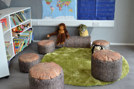 five stools that look like cut logs and one long one lying on the floor surround a furry rug creating a homely reading corner