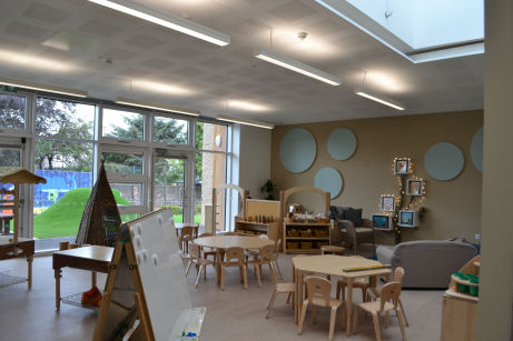 the nursery classroom is decorated like a home, with a sofa and fairy lights. circular pinboards are decorative on the wall.