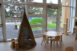 a teepee nook with a furry rug, beside a round table and chairs with a floor to ceiling view to the playground