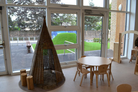 a teepee nook with a furry rug, beside a round table and chairs with a floor to ceiling view to the playground