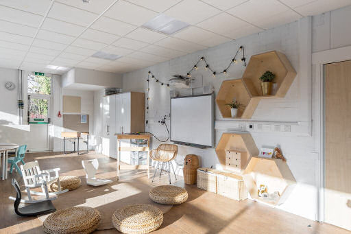 on the wall with the smart board are some fairy lights. a comfy adult chair is in front of it with a stand for a laptop. a circle of different seats surrounds the smart board