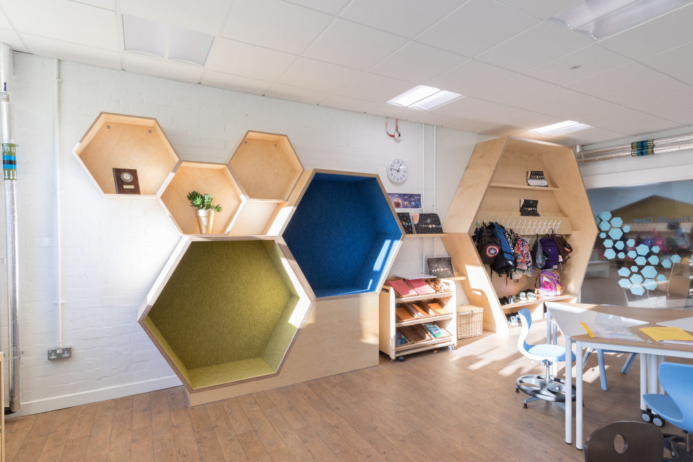 A close up of the hexagons on the wall. three small ones for display, two medium ones with green and blue upholstered interiors for sitting in and one large one used as a cloakroom. There is a big window to see into the breakout area which has a hexagon graphic on it that represents the stones of Fingals cave.