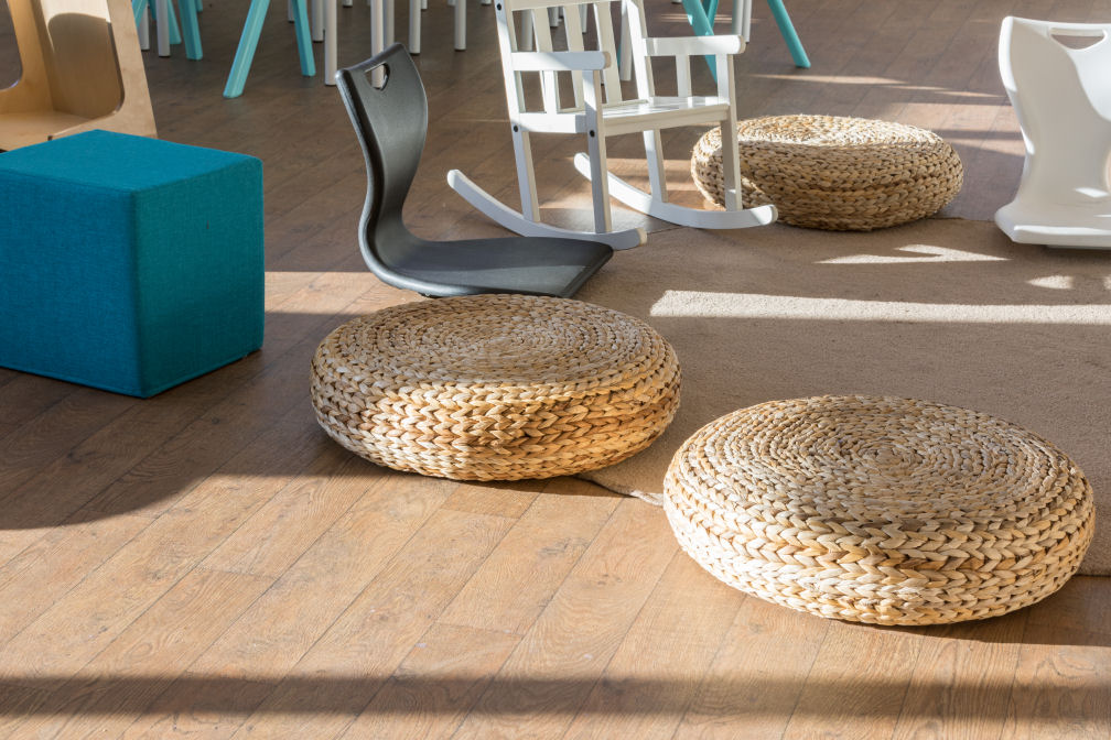A close up of the different seating options on the rug, three wicker seat pads, two floor rocking seats, a traditional rocking chair and a blue upholstered seat cube