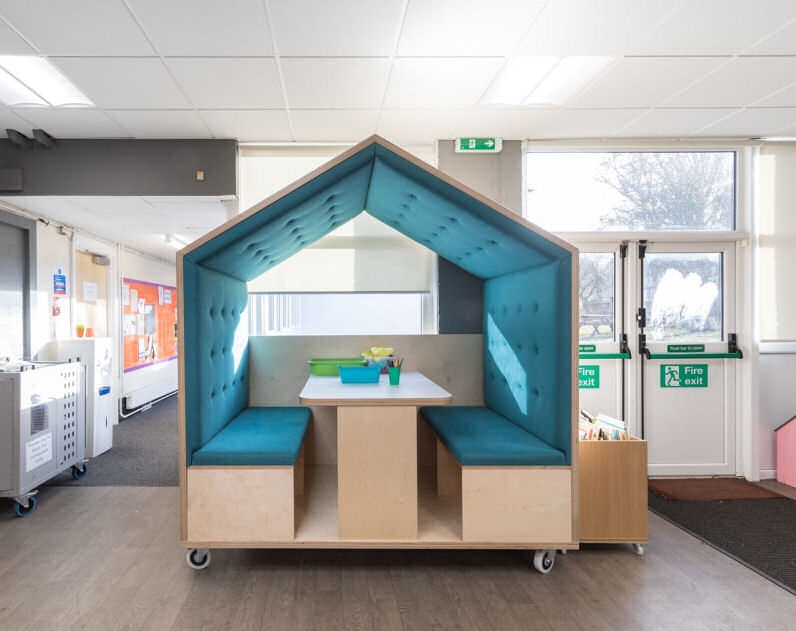 a house shaped meeting space on wheels, there are two benches facing each other over a table and gives a little privacy