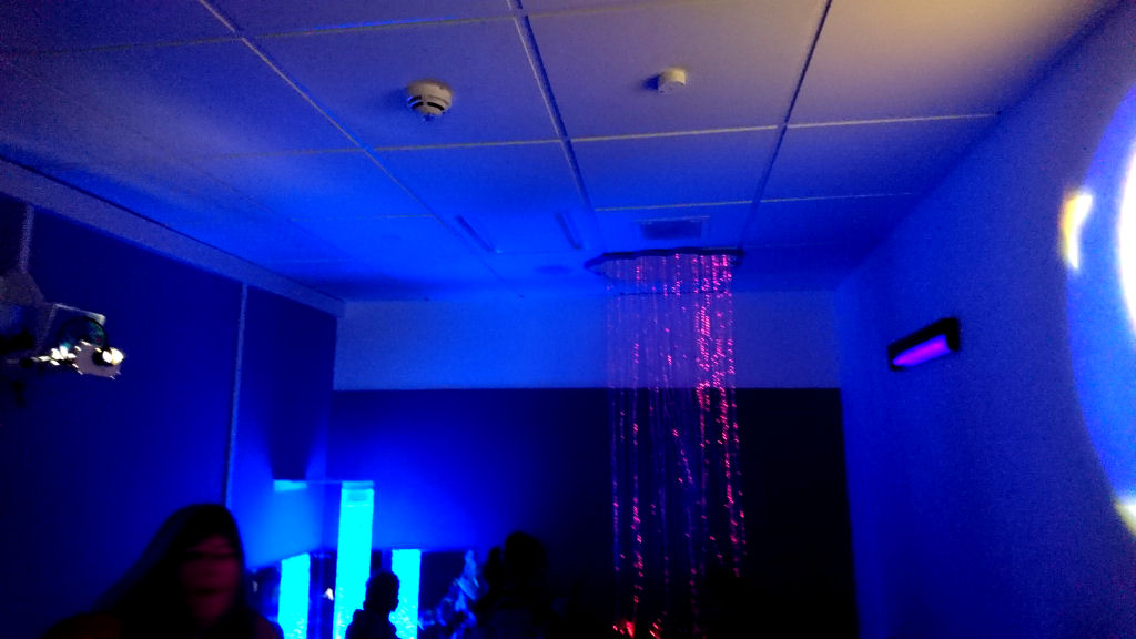 The sensory room is dark with UV lighting, a bubble tube and dangling lights and a fibre optic curtain