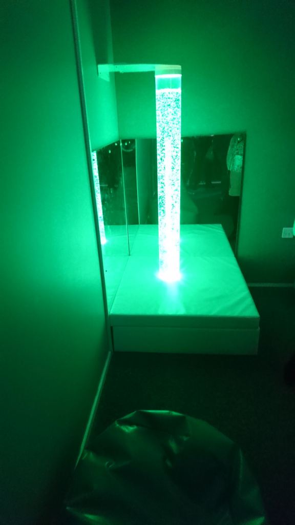 A green bubble lamp in the corner lights the area in green light, a beanbag is beside it