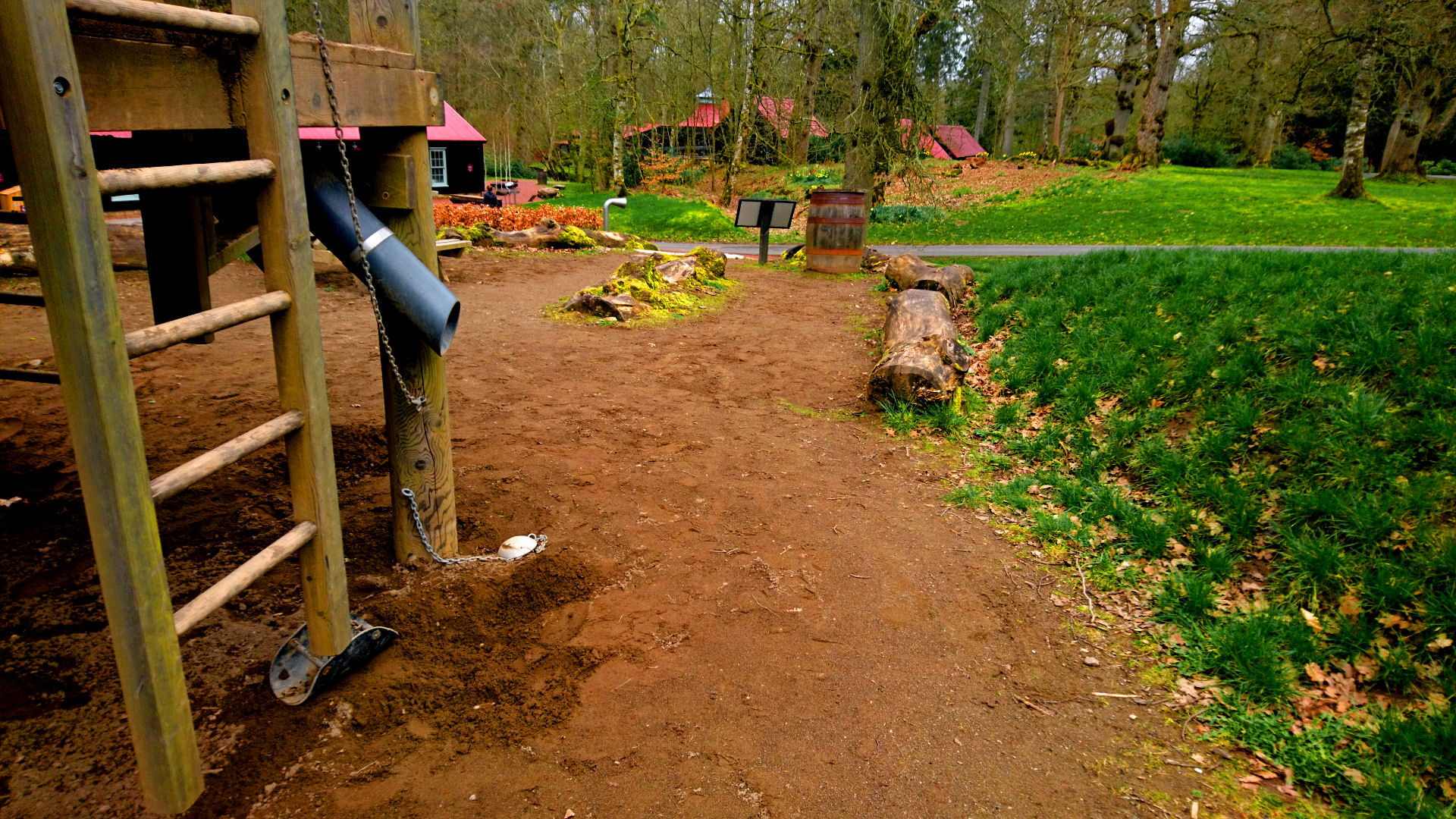 A timber structure with ladders, chutes and pulleys are in the sandpit. The sand is surrounded by grass