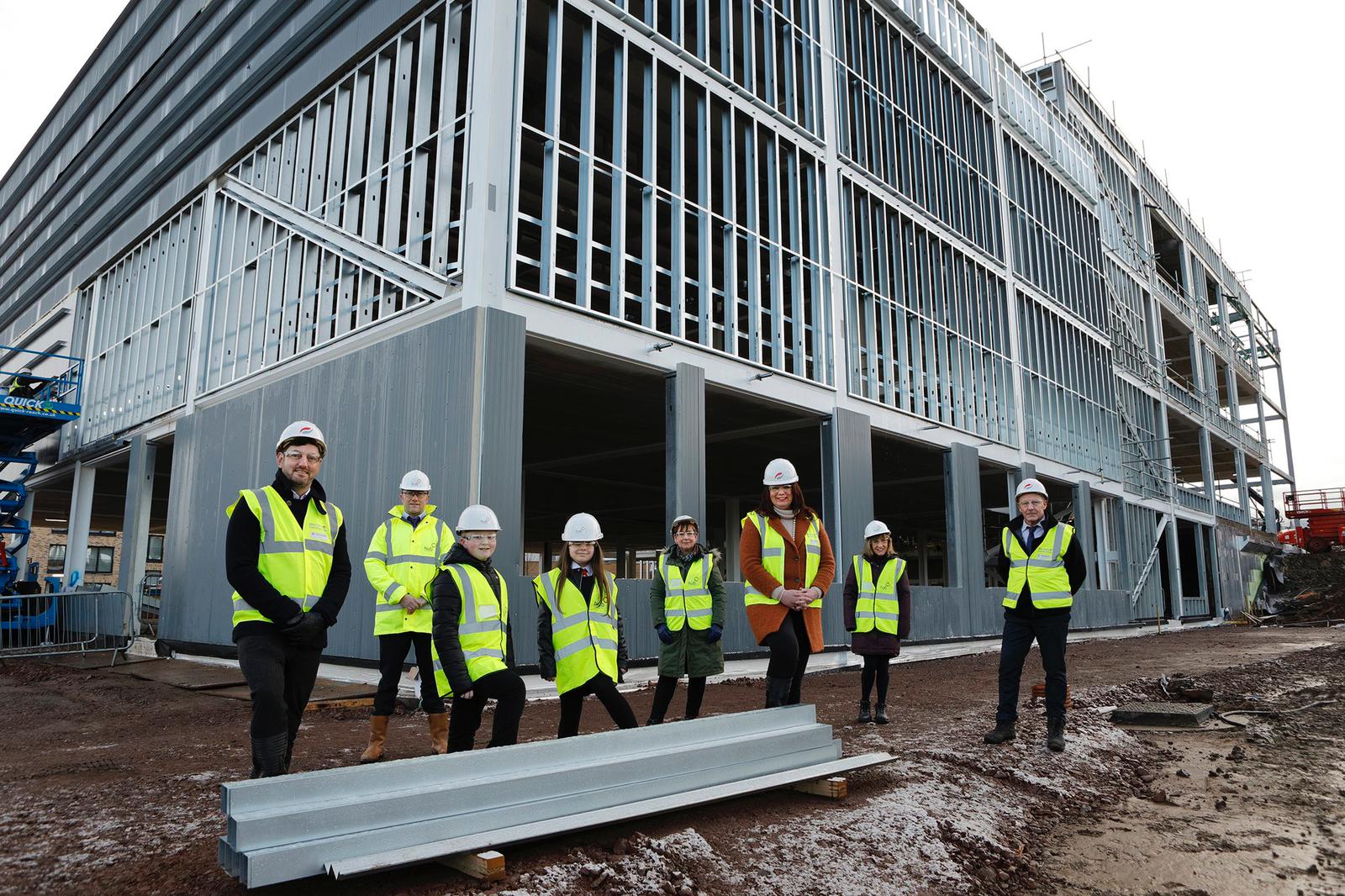 students and project team stand outside the new school in construction