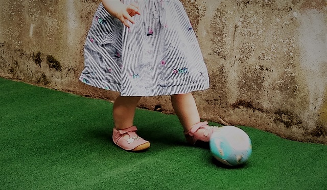 A child kicks a ball on some astroturf