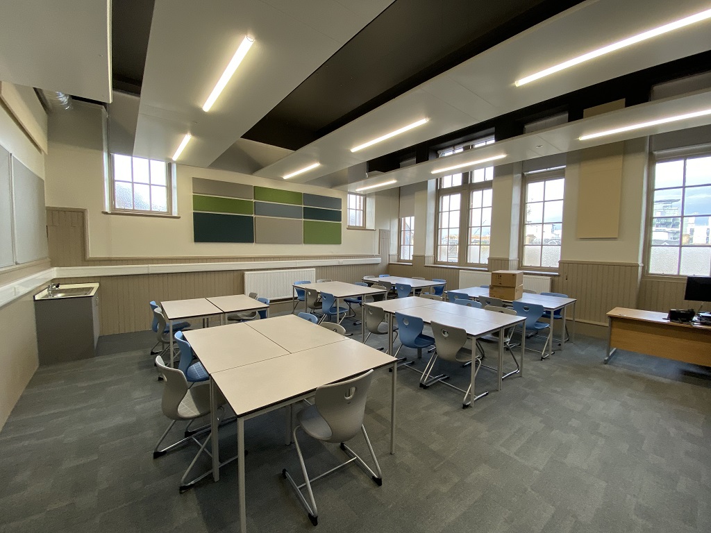 A classroom with small rectangular desks set up in different sized groups with modern chairs
