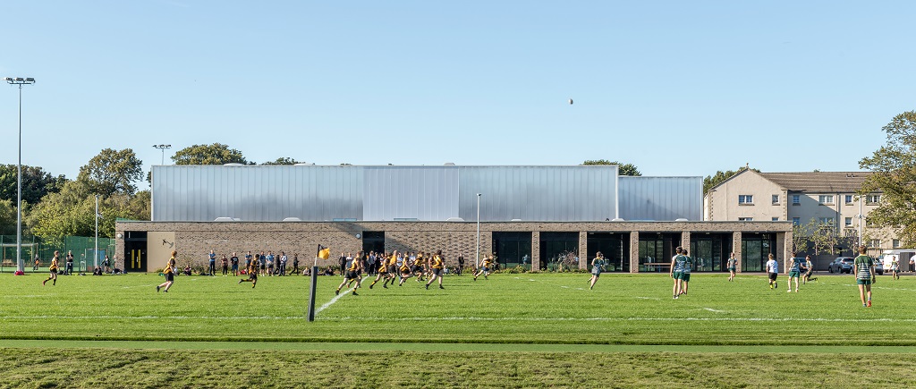View of the building from the corner of the site looking out across the rugby pitch, students are playing rugby