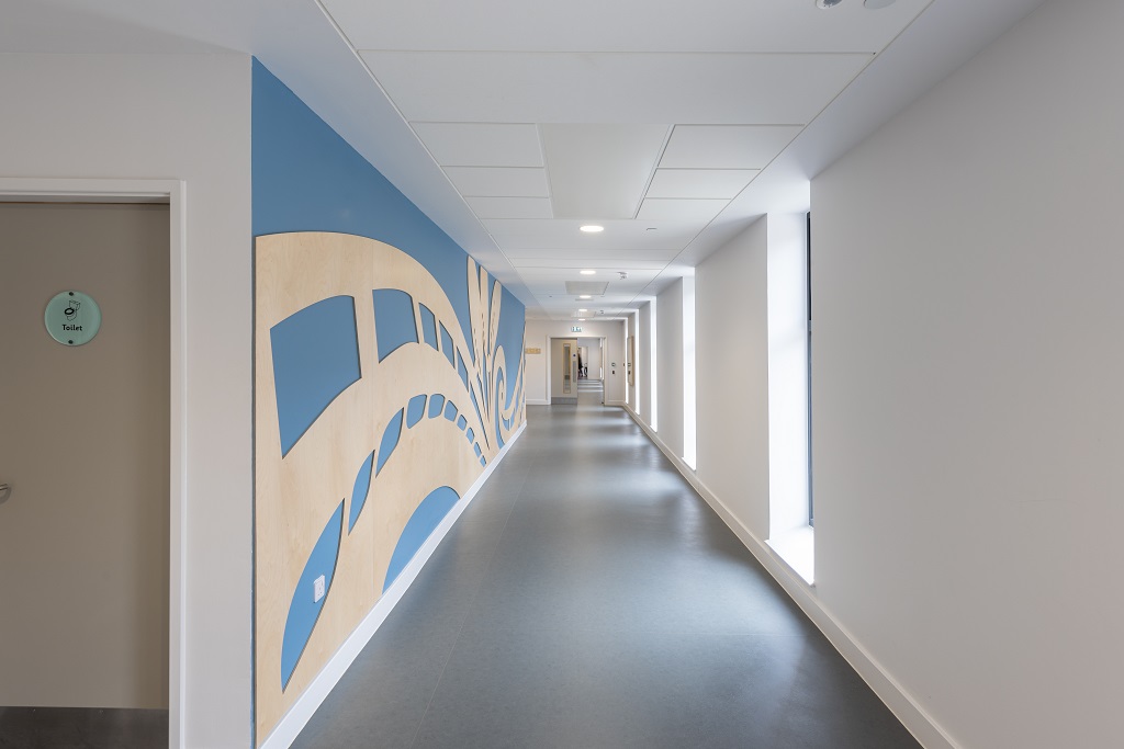 Corridor with grey flooring, the left wall is blue with natural wood cut out relief