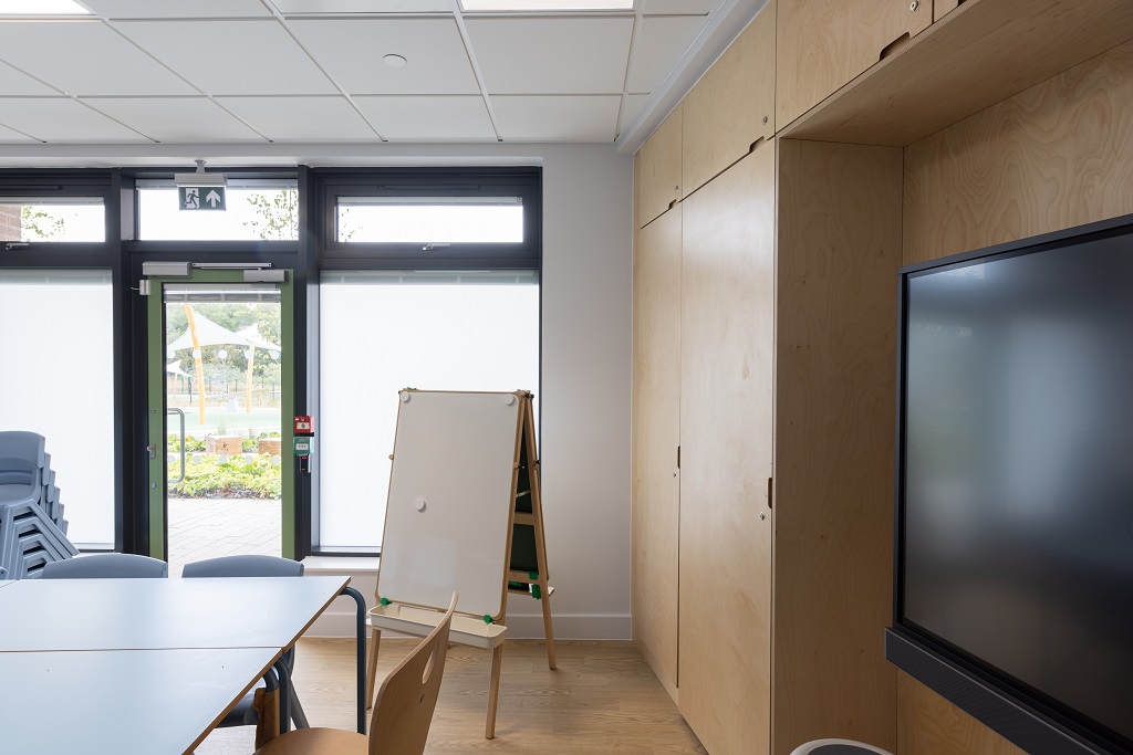 Corner of a classroom showing interactive screen on the wall, wooden storage cabinets and a portable white board