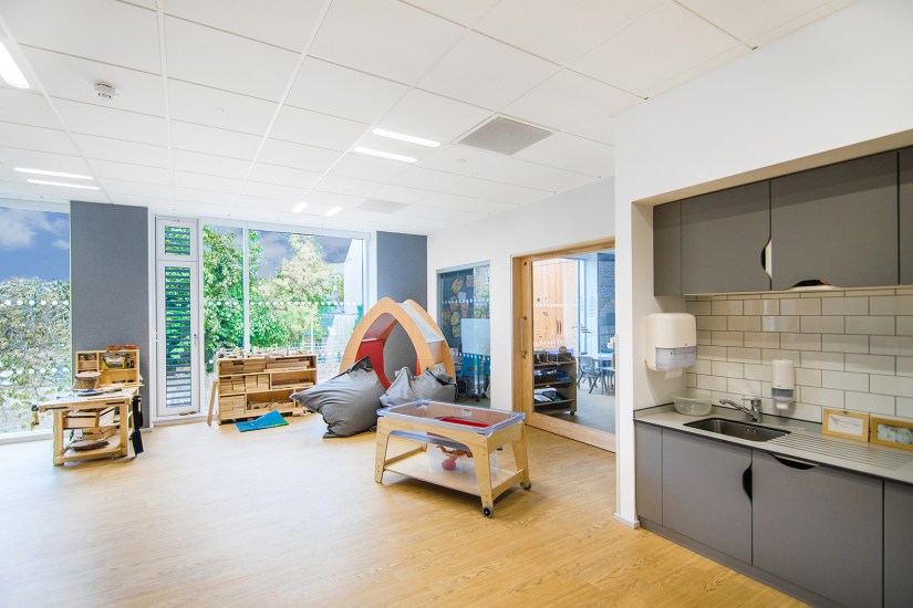 The nursery, with kitchenette in foreground, natural wooden furniture and play equipment, big cushions, floor to ceiling windows