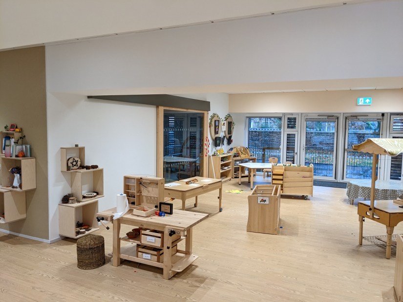 A neutrally decorated playroom, white walls and light wood flooring and furnishings