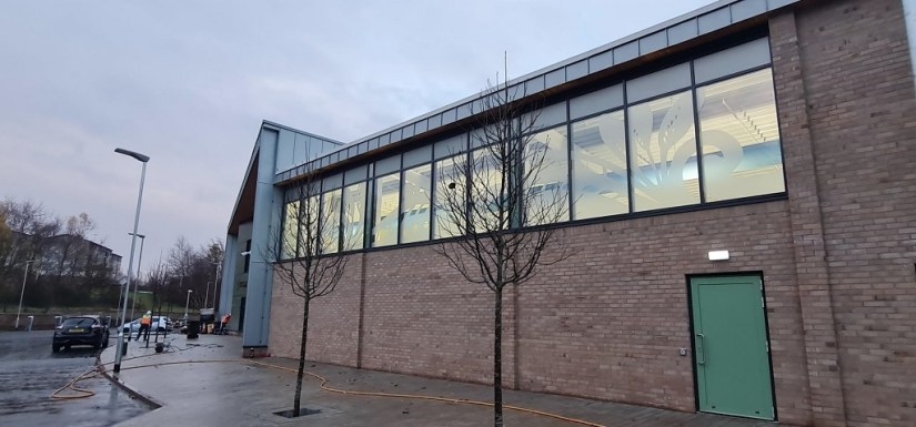 The school building exterior of the pool, with green door, brickwork and large windows at the top with a leaf design