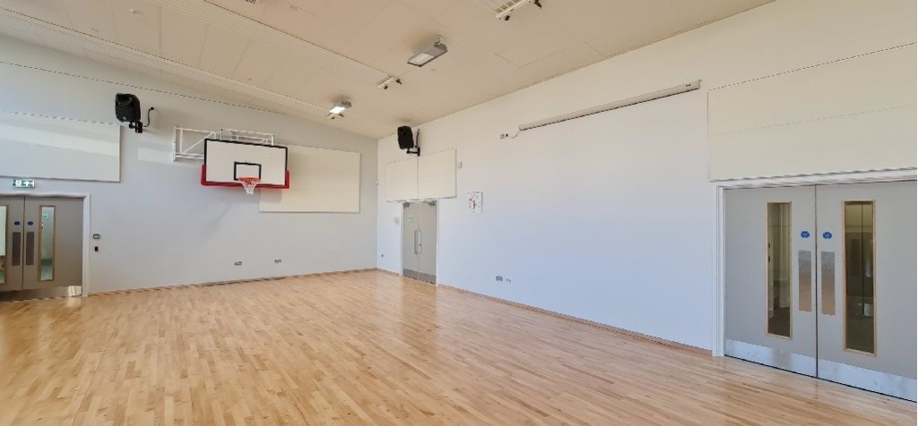 a gym hall with wooden floor and basketball hoop