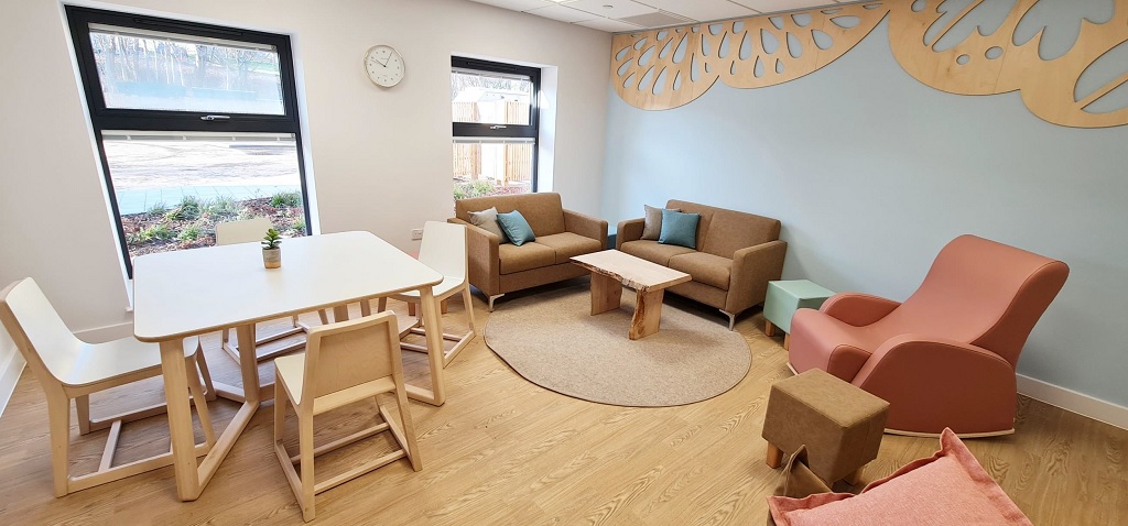 A homely room with two sofas in the corner beside a coffee table, a red upholstered rocking armchair, a square wooden table and chairs