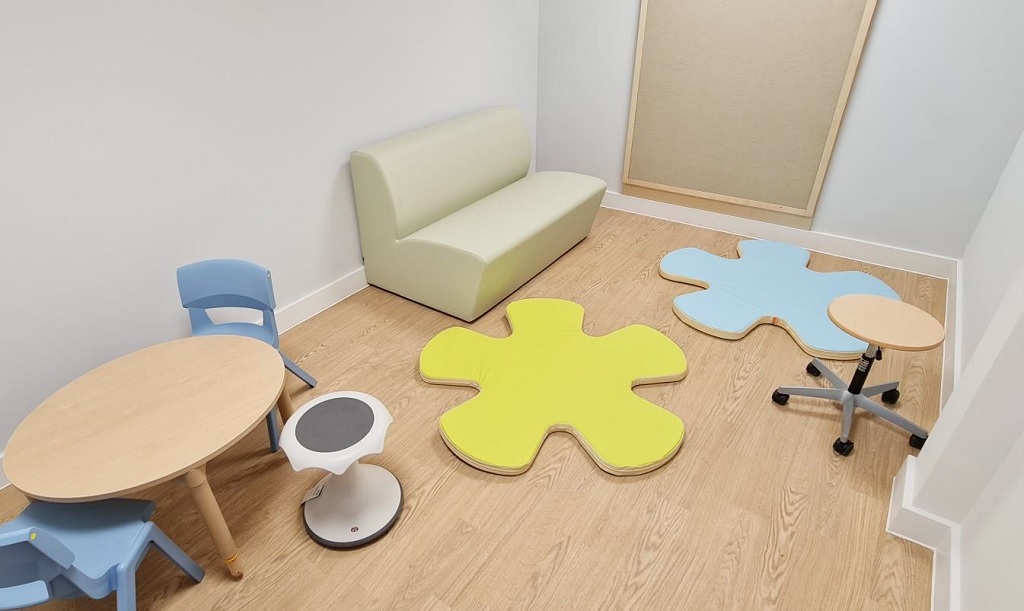A small room with sofa in the corner, round table and chairs and colourful flower shaped cushioned floor mats.