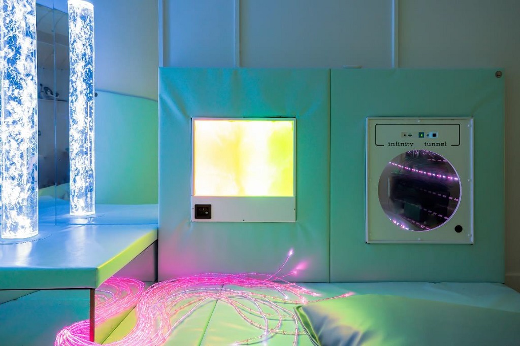 A light square panel and infinity tunnel are inset into the cushioned wall panels. lit LED strings and bubble lamp lit up in front of a mirror