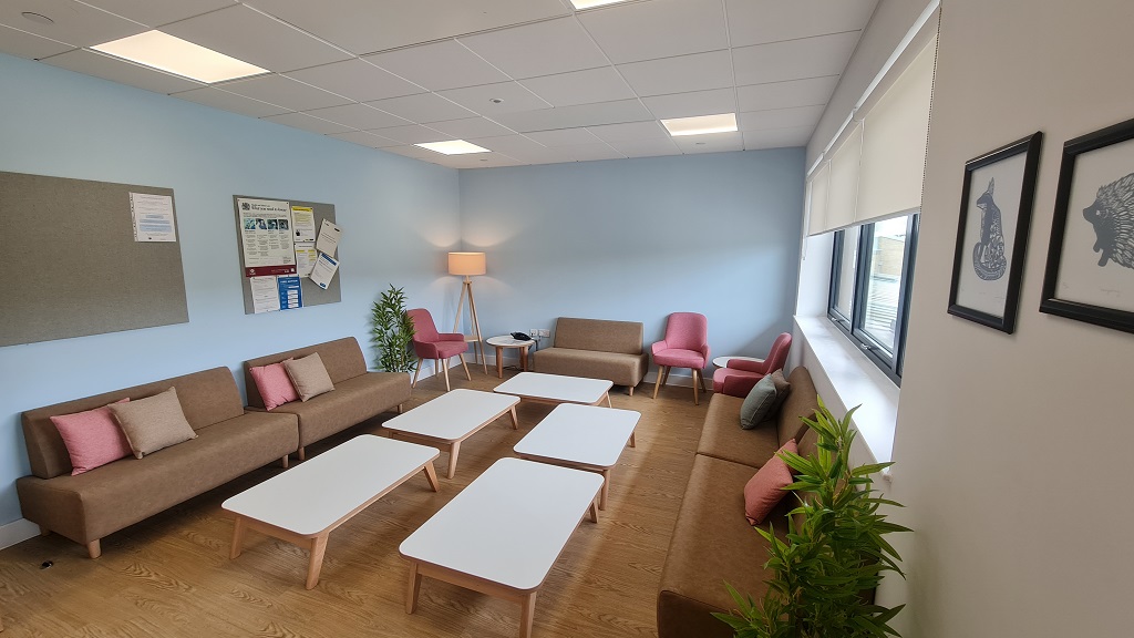 Sofas are positioned around the edge of the room, a few upholstered chairs are the the far end and five coffee tables are in the centre