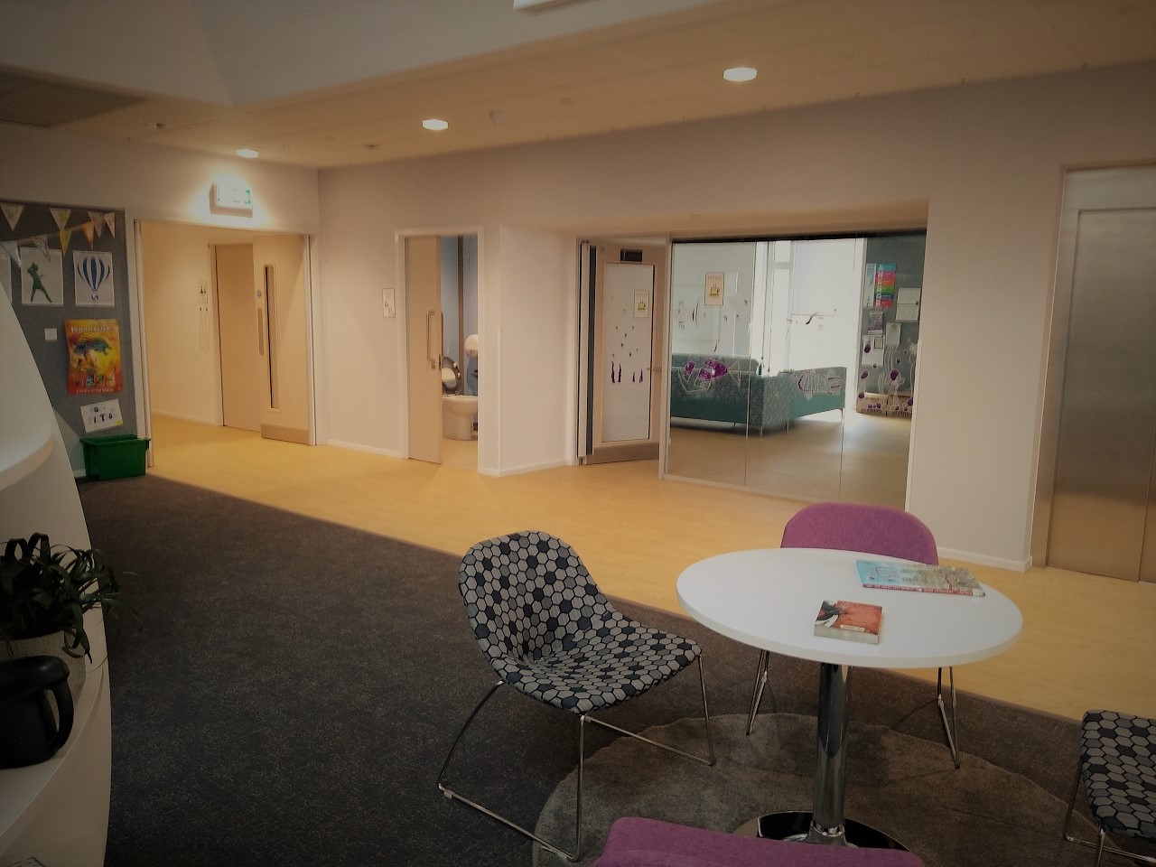 a circular white table with four upholstered chairs, open to a corridor leading to classrooms