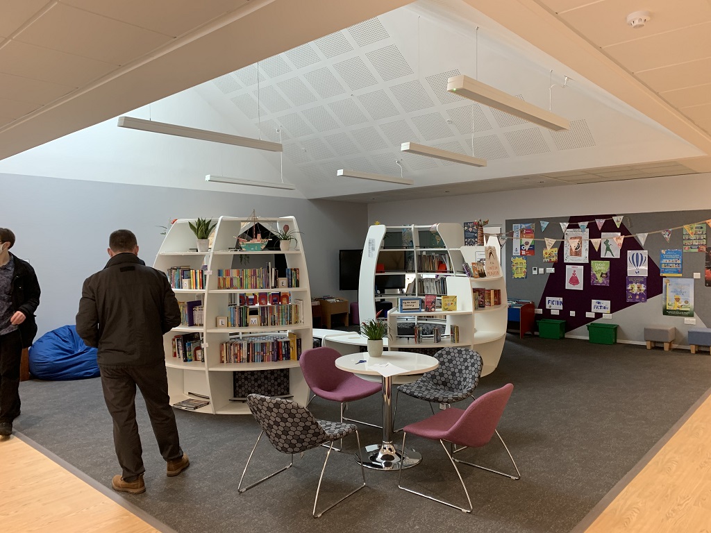 people stand in a library with curved bookcases and comfy seats