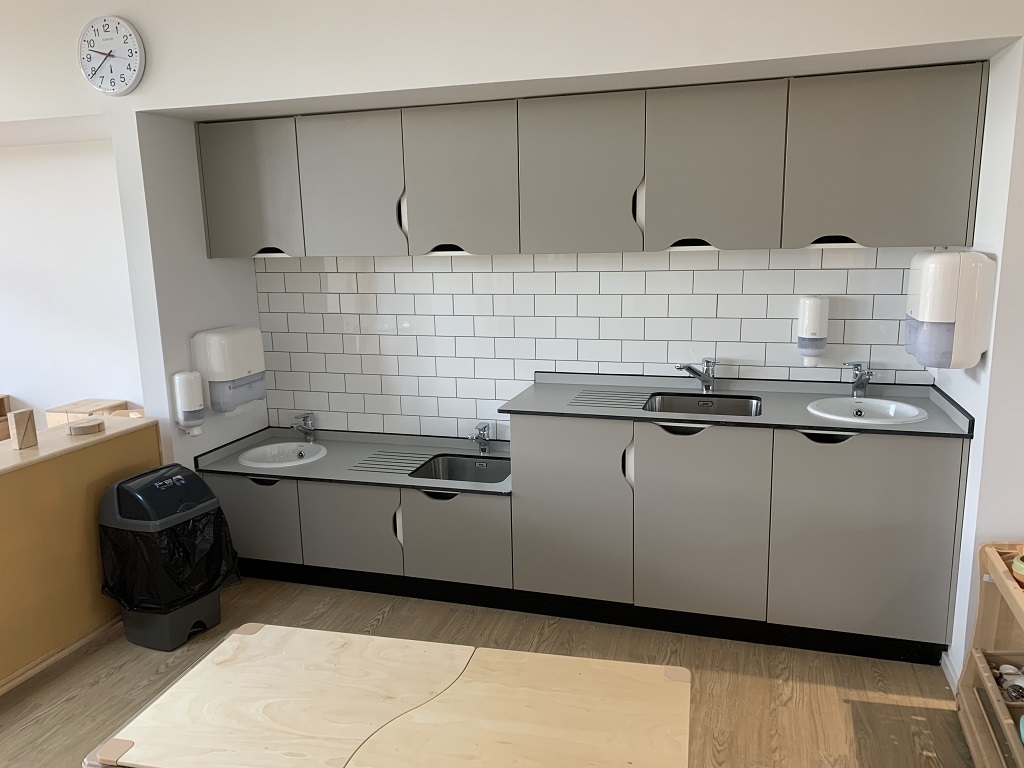 a small prep kitchen in the nursery, grey units with sinks for adults and children and white tiles