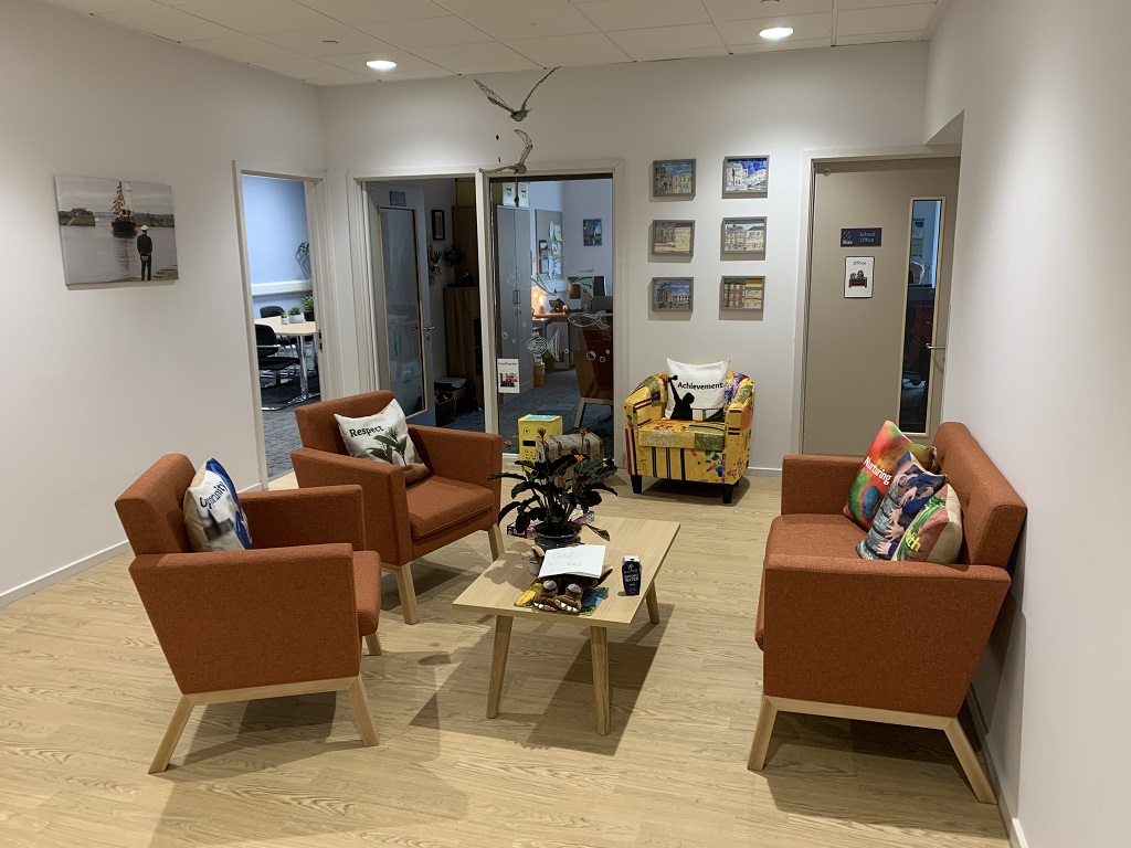 a waiting area with homely furnishings, orange sofa and armchairs, coffee table and plant