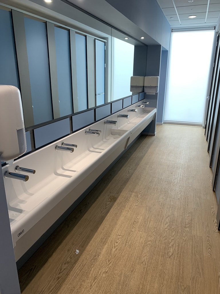 bathroom with a low level sink trough along one side and cubicles on the other